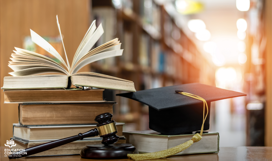 A stack of books, a gavel and a graduation cap sit on a table inside a library to represent expanding education access and graduation opportunities for people impacted by the justice system.
