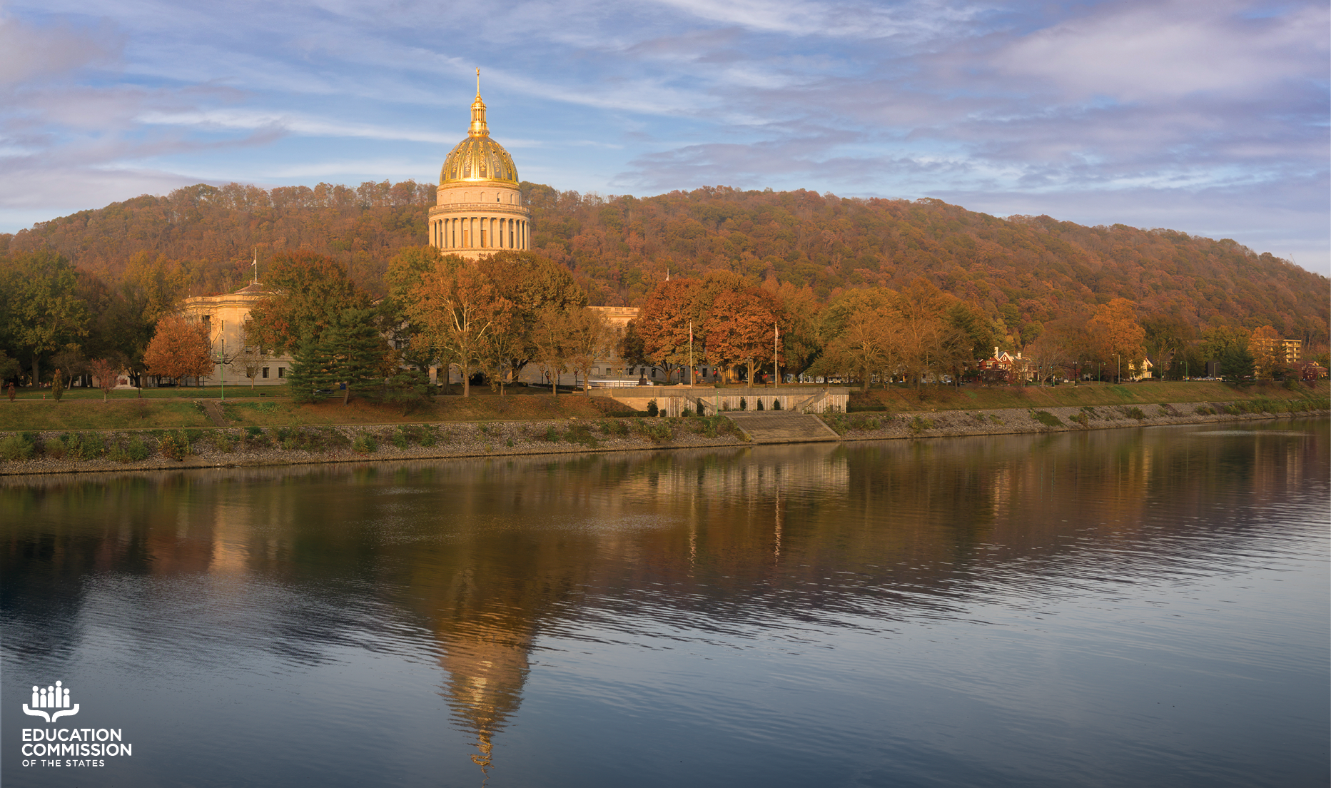 The West Virginia state capitol building around sunset. The capitol's reflection is captured in the Kanawha River below.