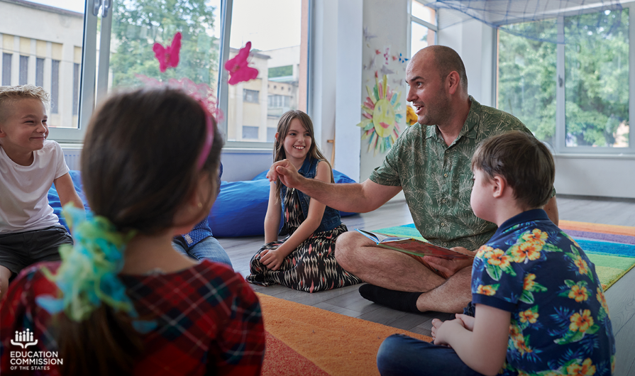 Several young students in a special education class sit in a circle while a teacher reads and acts out a story.